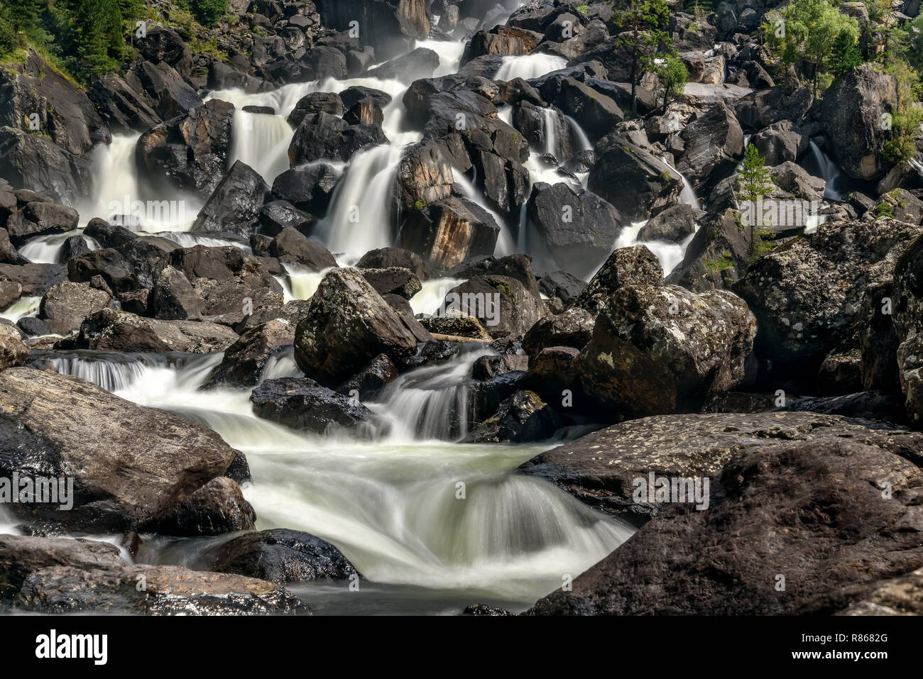 Bella cascata con acqua liscia che rientrano tra le rocce e pietre nere in montagna, girato con una lunga esposizione Foto Stock