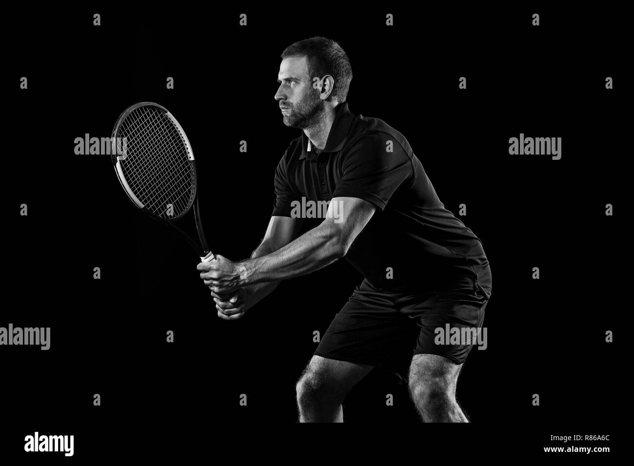 Un uomo caucasico giocando a tennis isolati su sfondo nero. Studio shot monocromatica di montare il giovane giocatore di studio in movimento o il movimento durante il gioco di sport. Foto Stock