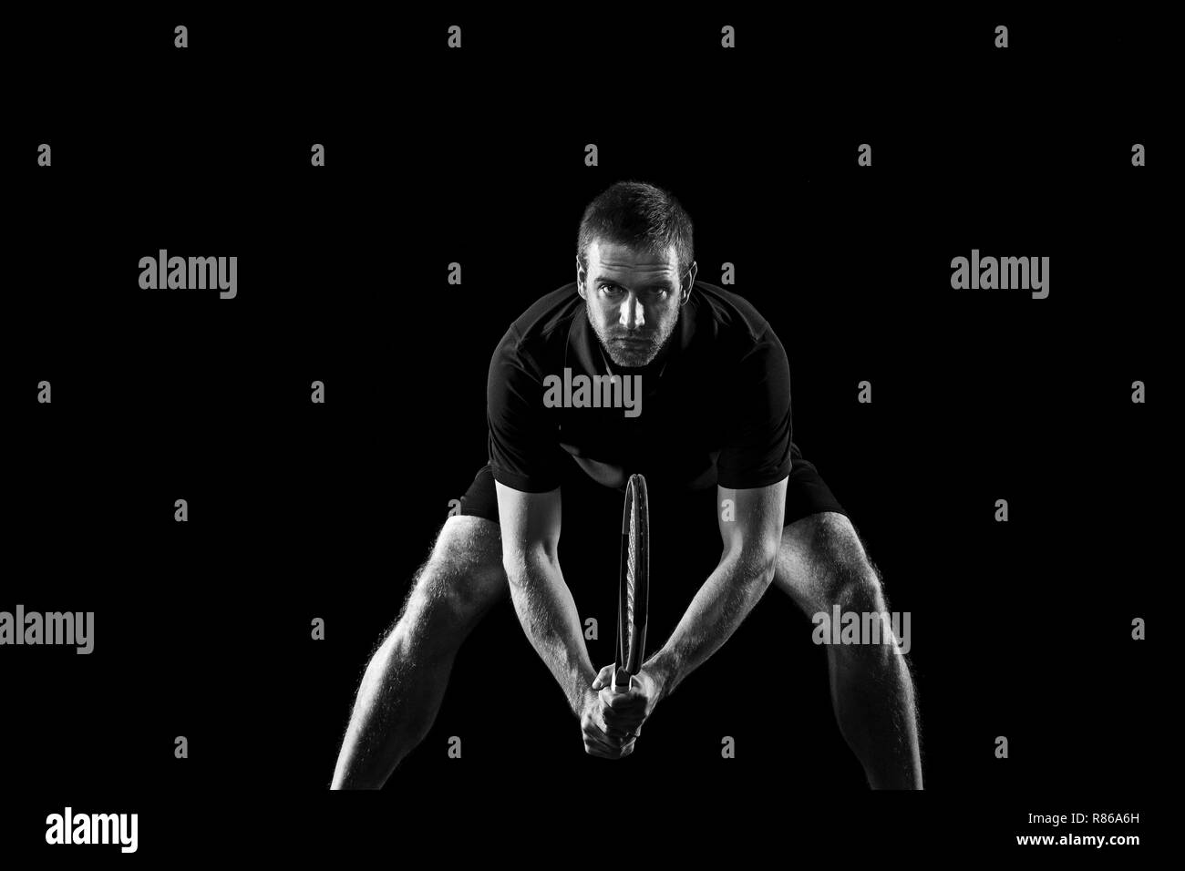 Un uomo caucasico giocando a tennis isolati su sfondo nero. Studio shot monocromatica di montare il giovane giocatore di studio in movimento o il movimento durante il gioco di sport. Foto Stock