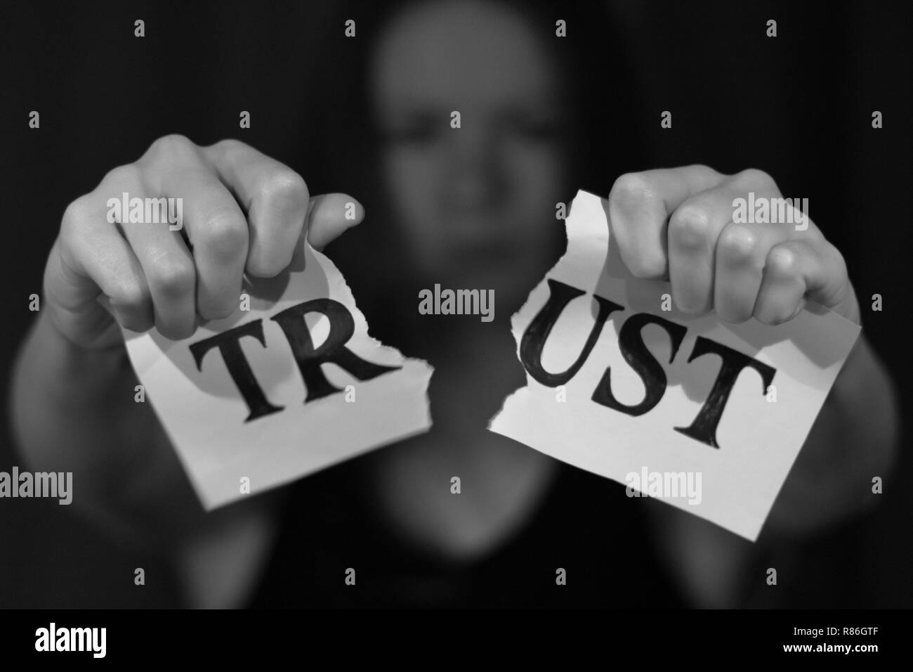 Strappato carta bianca con disegnato lettere di 'fiducia'. Ragazza strappando la carta in due metà. Foto Stock