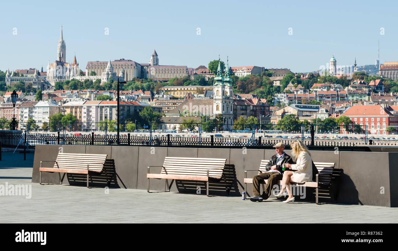 Un giovane seduto su una panchina vicino al parlamento ungherese, con il castello di Buda Hill in background, Budapest, Ungheria Foto Stock