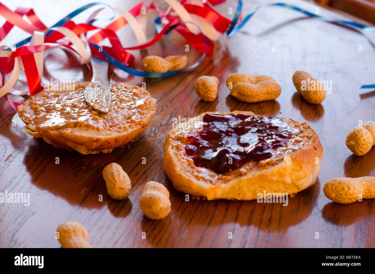 Burro di arachidi e jelly sandwich con tutta le arachidi sparsi sul tavolo con rosso, bianco e blu bande in background. Foto Stock