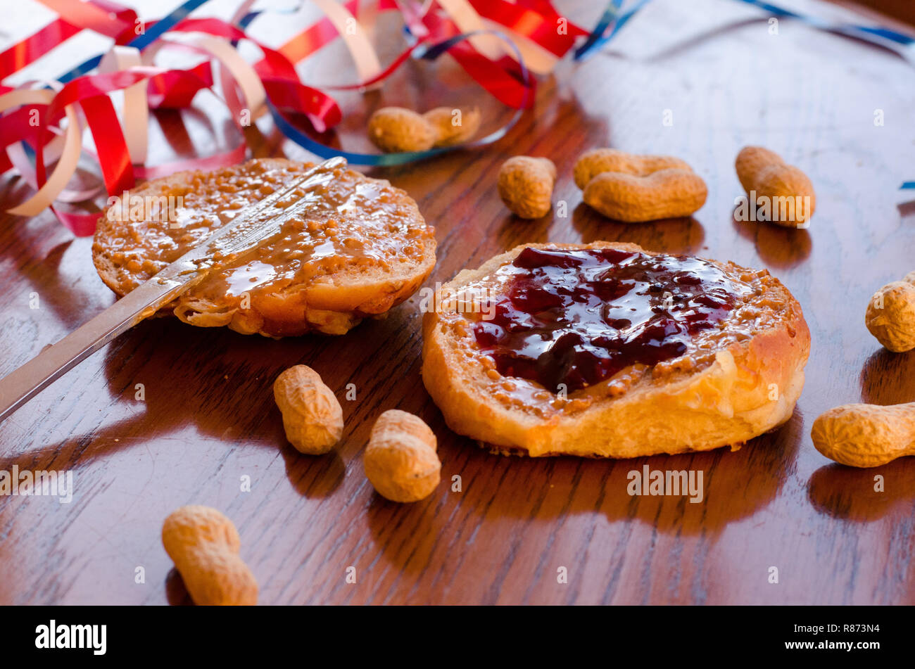 Burro di arachidi e jelly sandwich con tutta le arachidi sparsi sul tavolo con rosso, bianco e blu bande in background. Foto Stock