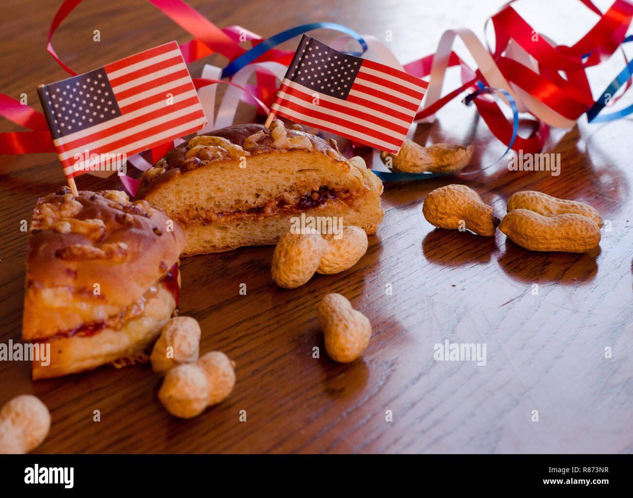 Burro di arachidi e jelly sandwich con bandierine americane imperniata ad essa e tutta le arachidi sparsi sul tavolo con rosso, bianco e blu in bande backgrou Foto Stock