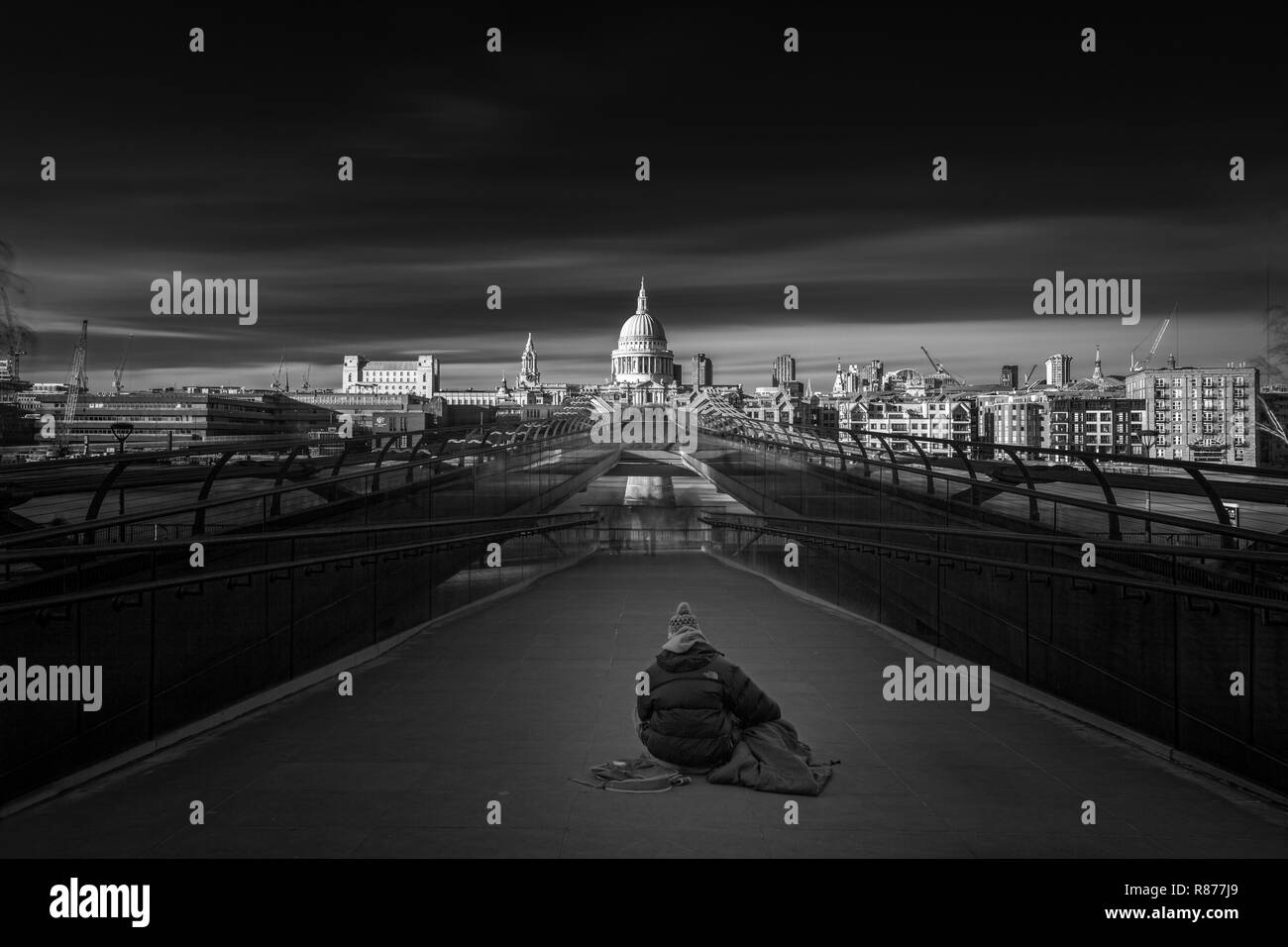 Senzatetto persona seduta sul Millennium bridge guardando verso St Pauls nella città di Londra Foto Stock