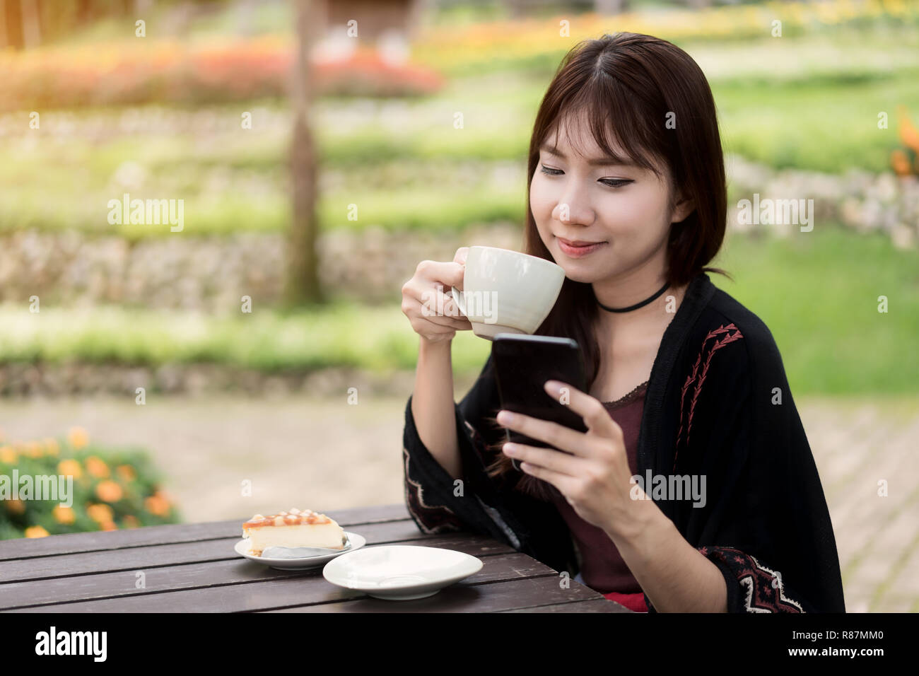 Belle Donne asiatiche hanno goduto nel giardino con caffè e chiacchierare in smartphone. Foto Stock