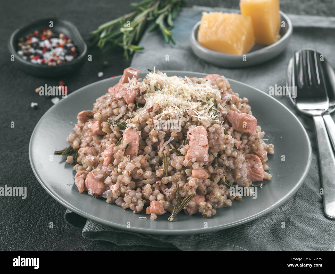 Materie del grano saraceno risotto con carne di pollo e il rosmarino servita parmigiano reggiano in lastra grigia su nero lo sfondo di cemento. Senza glutine e grano saraceno ricetta idee. Copia dello spazio. Tonica immagine. Foto Stock