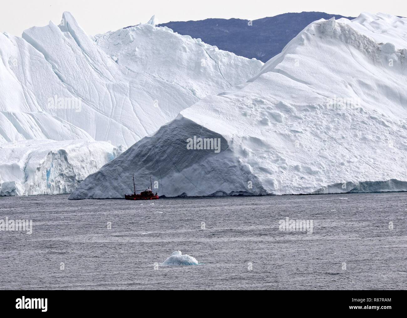 Grönland Disko Bucht: Landschaft mit Eisbergen Kleines rotes Ausflugsboot vor mächtigem Eisberg Foto Stock