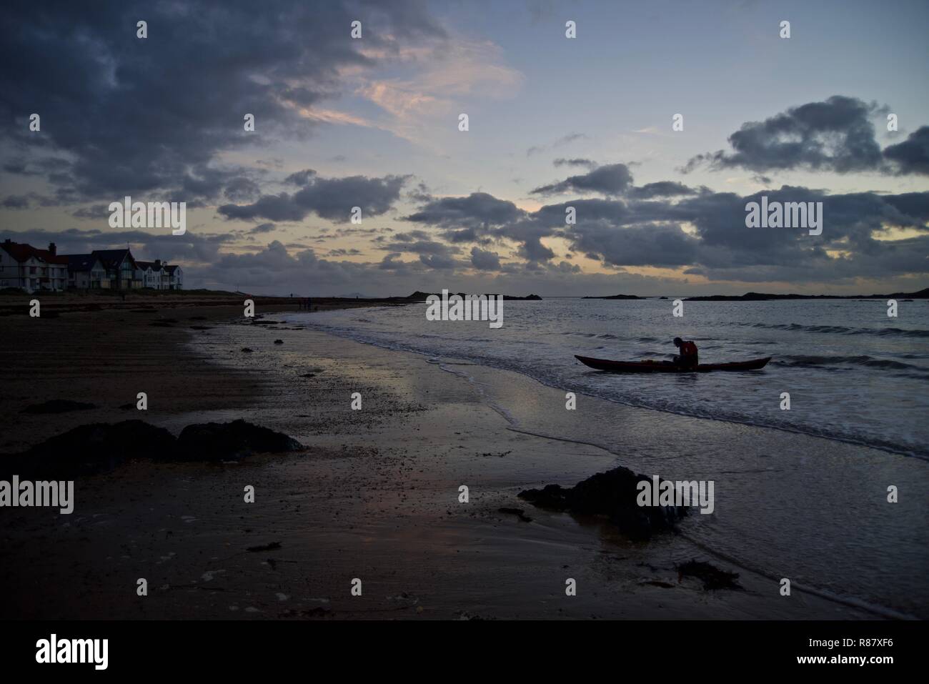 Un canoeist arriva a terra al tramonto nel villaggio di Rhosneigr, Anglesey, Galles del Nord, Regno Unito Foto Stock