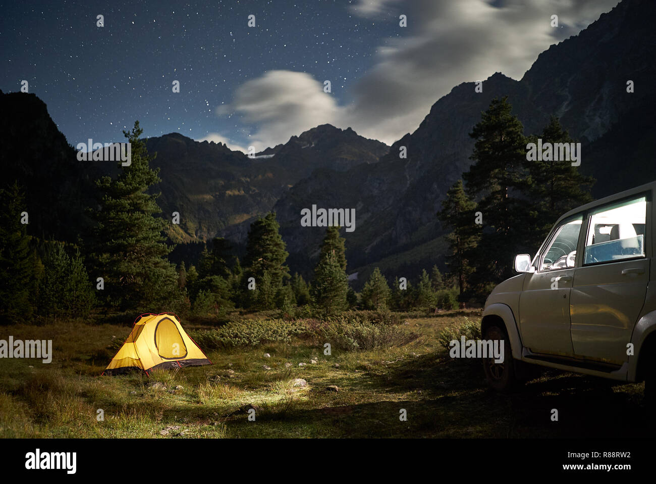 Camping con una vettura, giallo tenda di notte con il chiaro di luna in zona di montagna Foto Stock