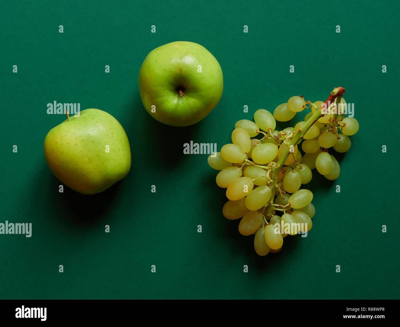 Vista al di sopra del gruppo isolato di una mela verde con un mucchio di dolci uve senza semi in studio con sfondo verde Foto Stock