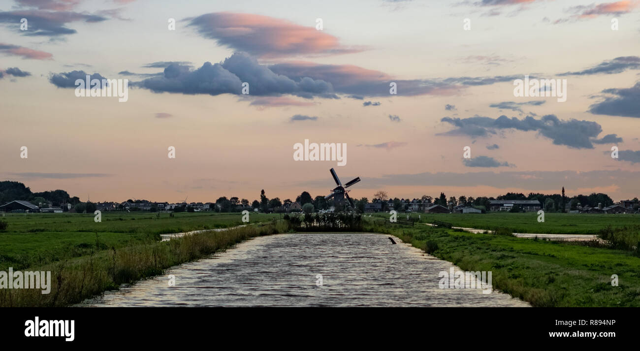 Canal con un vecchio mulino a vento olandese all'orizzonte sotto un cielo colorato. Tradizionale scena olandese, che può essere trovato nella parte occidentale del paese. Foto Stock