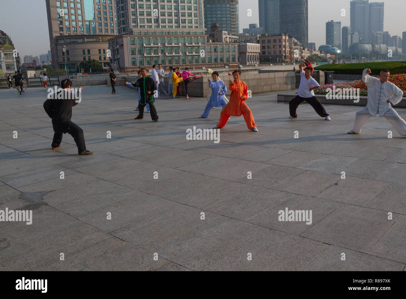 Persone che praticano arti marziali al sorgere di fronte lo skyline di Pudong di Shanghai, Cina. I partecipanti indossino colorato arti marziali abbigliamento. Foto Stock