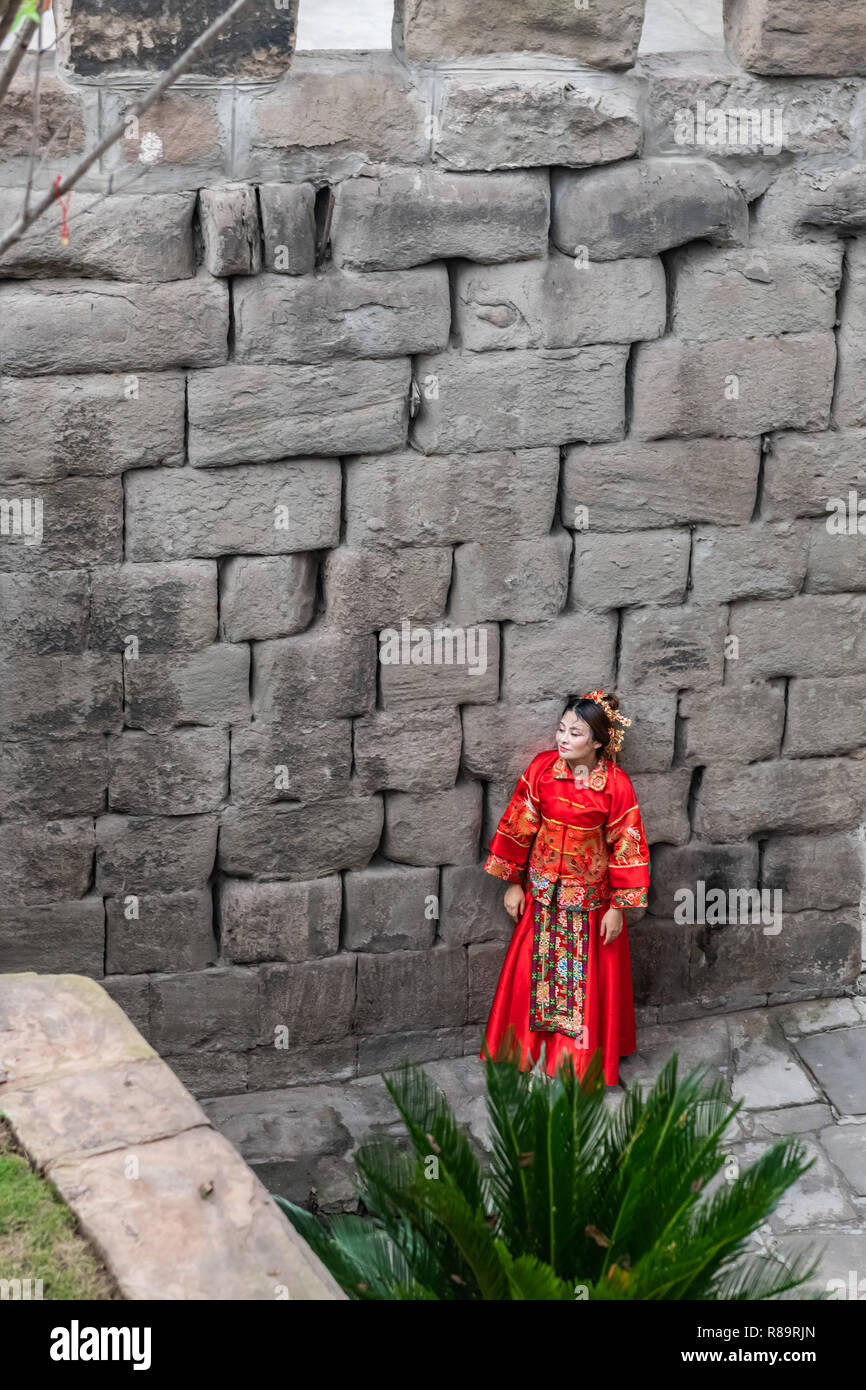 Donna in abito rosso - donna cinese in costume tradizionale in posa di Chongquing vicino alla parete del porto. Foto Stock