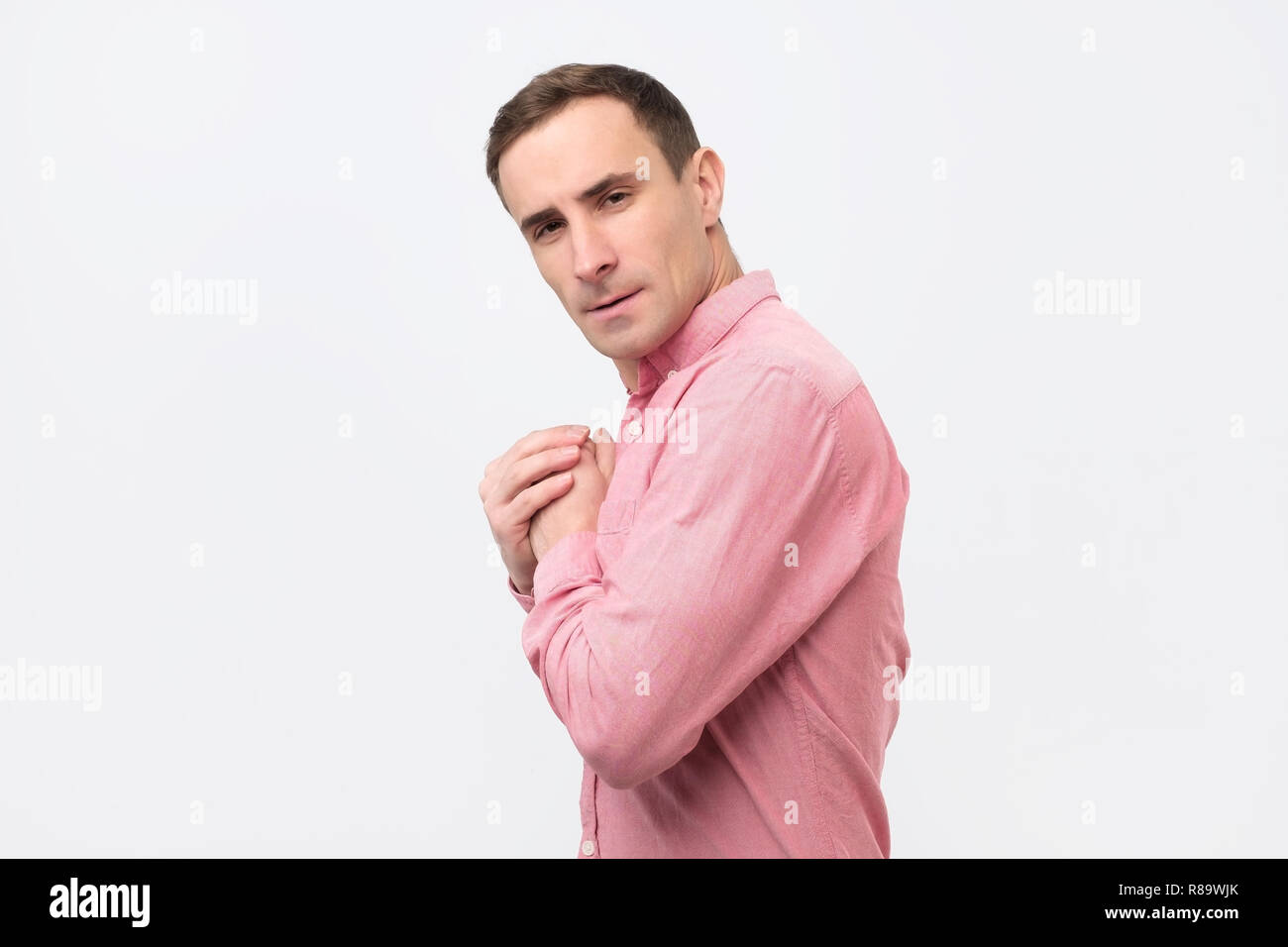 Un giovane uomo avido in maglia rosa nasconde qualcosa nelle sue mani Foto Stock