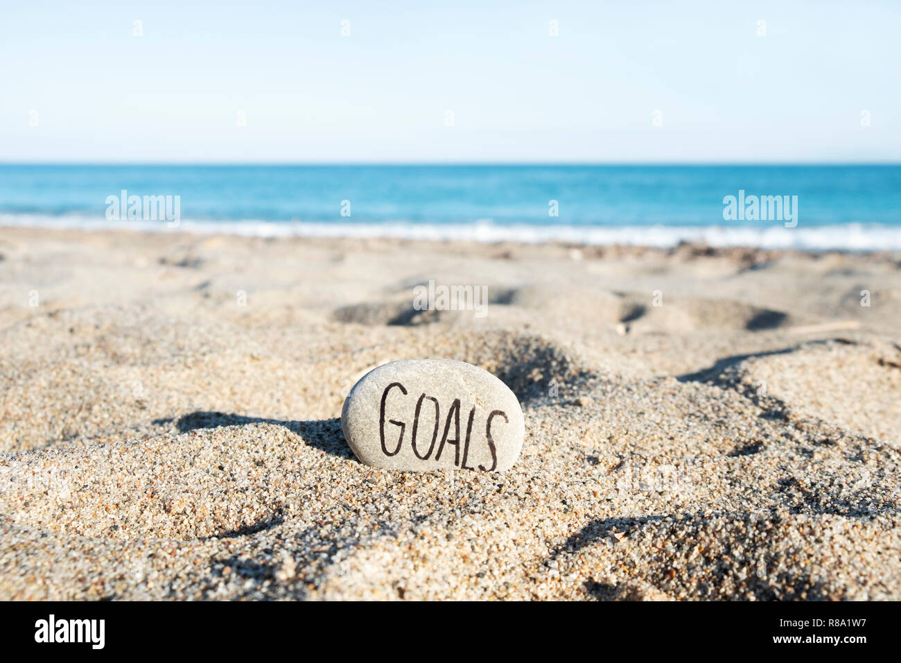 Primo piano di una pietra, con il testo scritto a mano gli obiettivi in esso, sulla sabbia di una spiaggia solitaria, con l'oceano sullo sfondo Foto Stock
