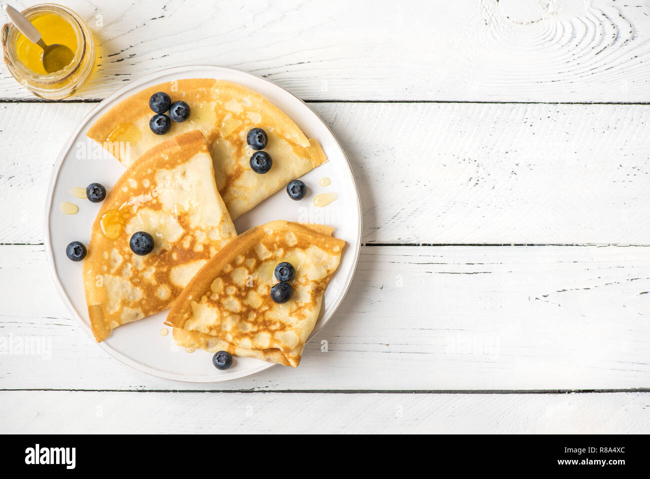 Crepes con mirtilli e miele. Frittelle fatte in casa, crepes su bianco tavolo in legno, copia dello spazio. Foto Stock