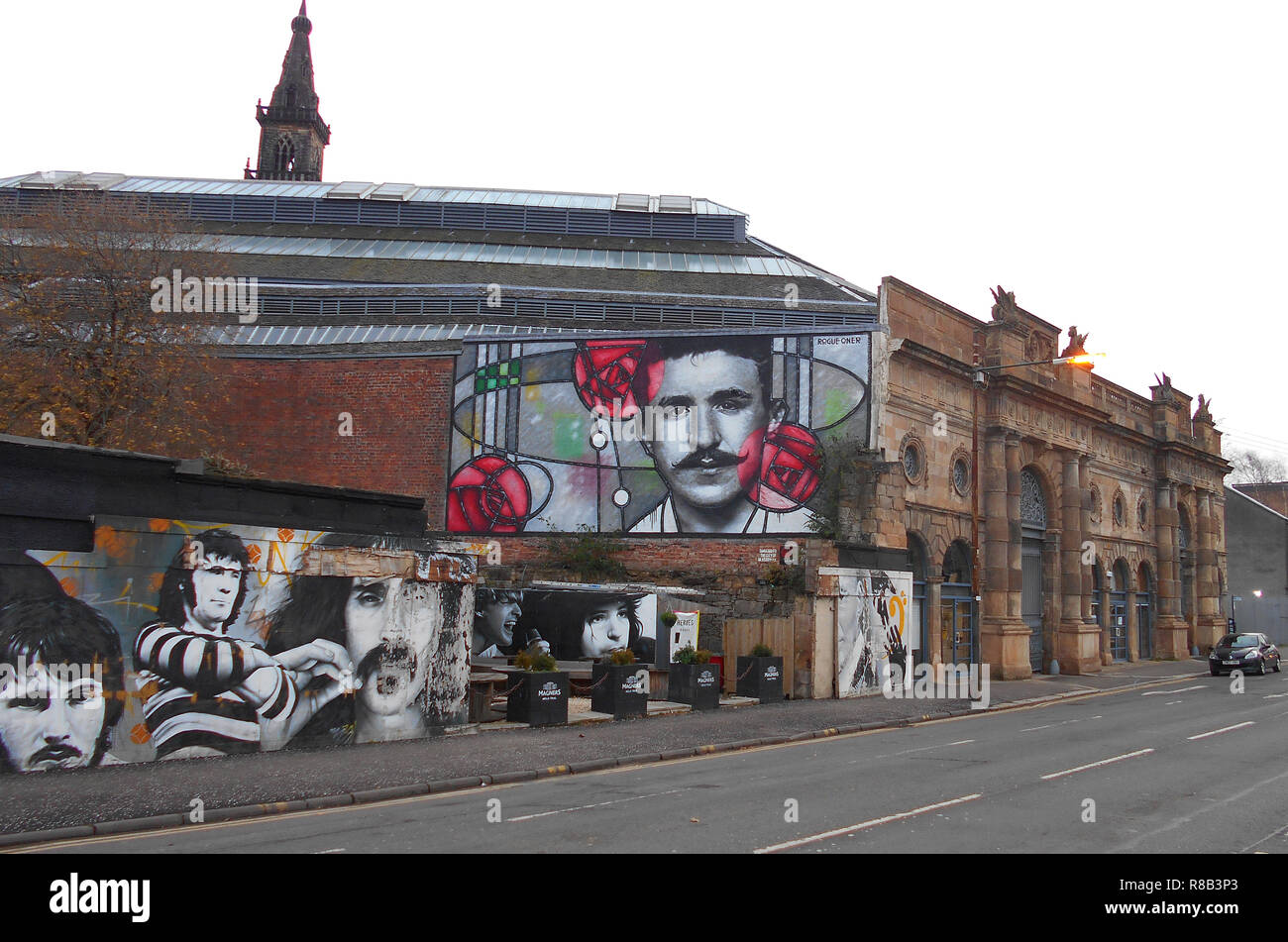 Questo grande e nuovo e splendido murale è apparso su un muro vicino al Clutha Bar, accanto al fiume Clyde a Glasgow, nel 2018. È il famoso architetto scozzese e designer Charles Rennie Mackintosh, e si commemora il centocinquantesimo anniversario della sua nascita nel 1868. Egli guarda giù sul murales di musicisti, Gerry Rafferty, Alex Harvey, Frank Zappa e Frankie Miller! Alan Wylie/ALAMY © Foto Stock