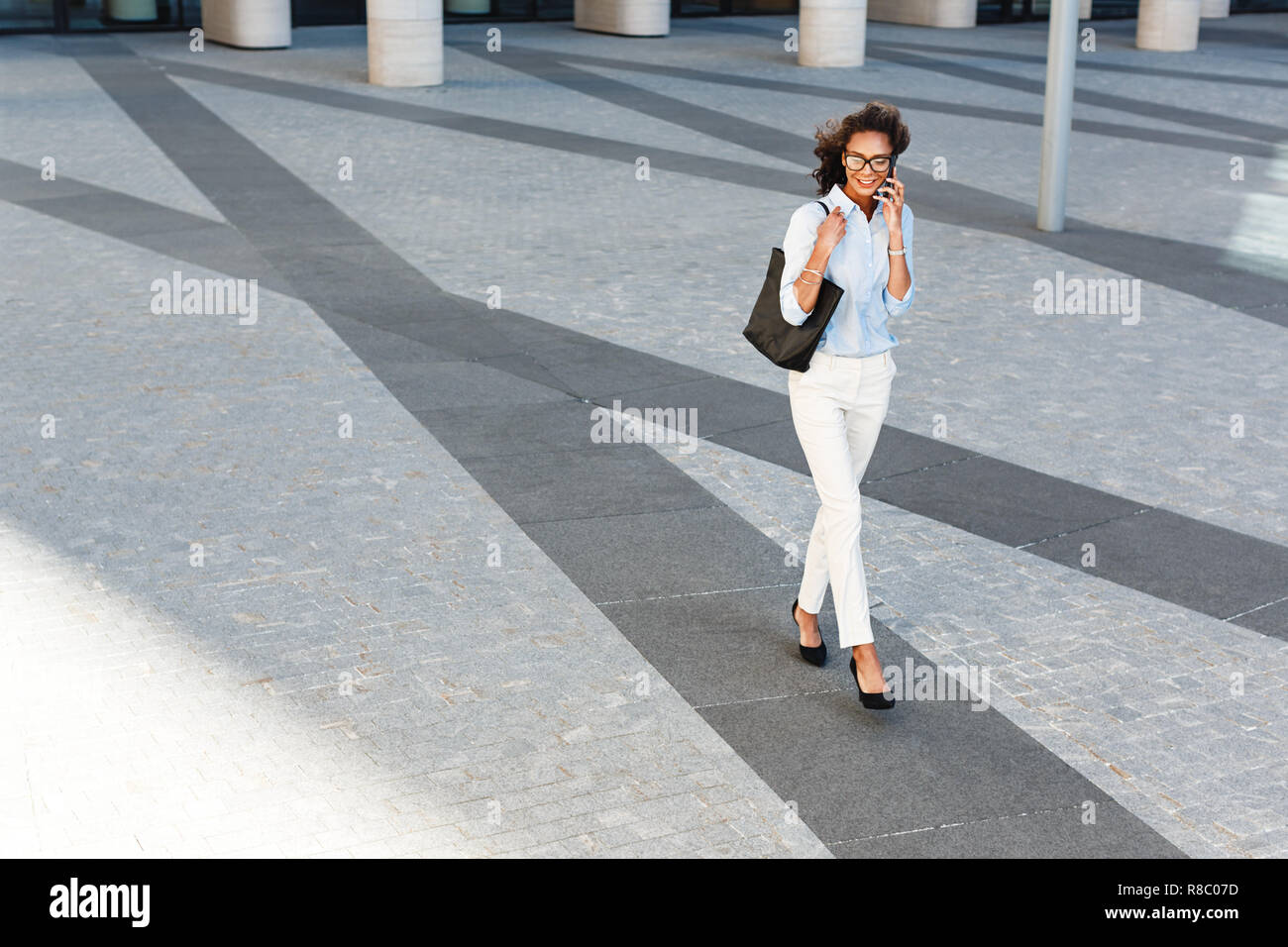 Giovane donna camminare al di fuori sulla strada di città, parlando al telefono cellulare Foto Stock