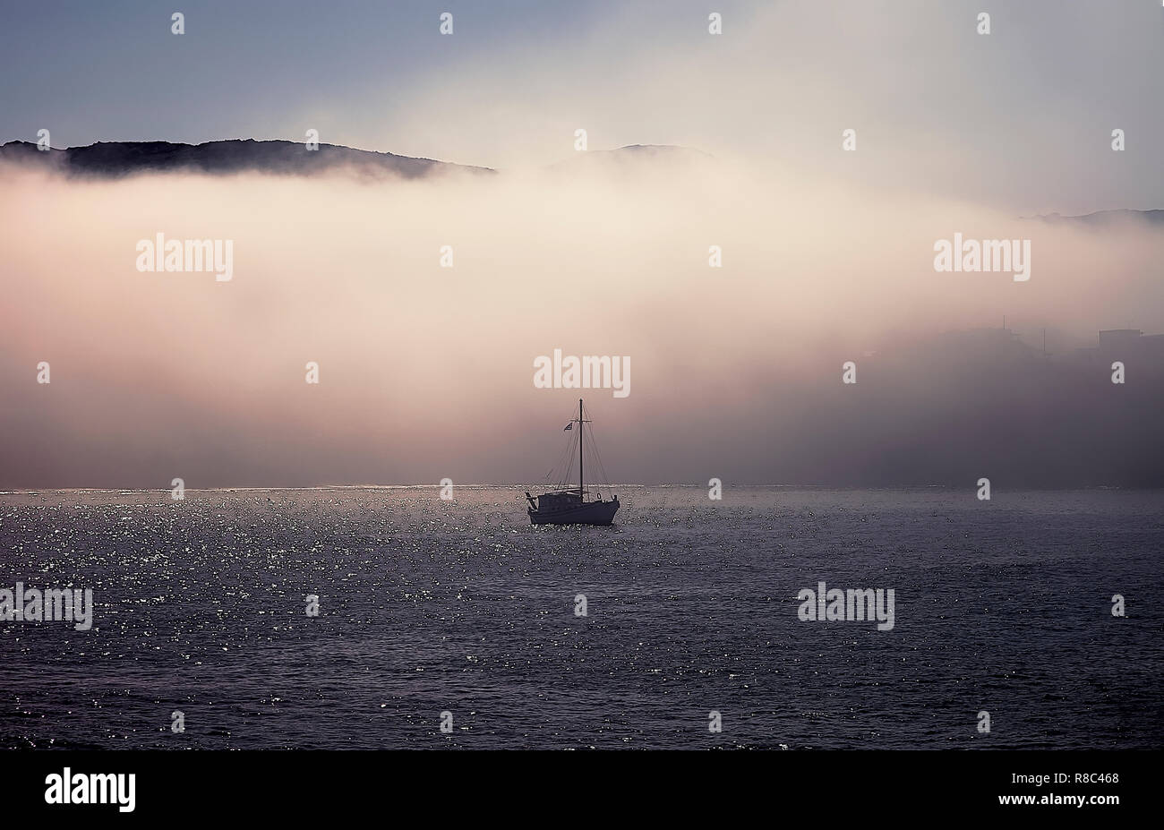 Barca da pesca di prima mattina entrando nella baia di Finikas nella fitta nebbia. Immagine di stock. Foto Stock