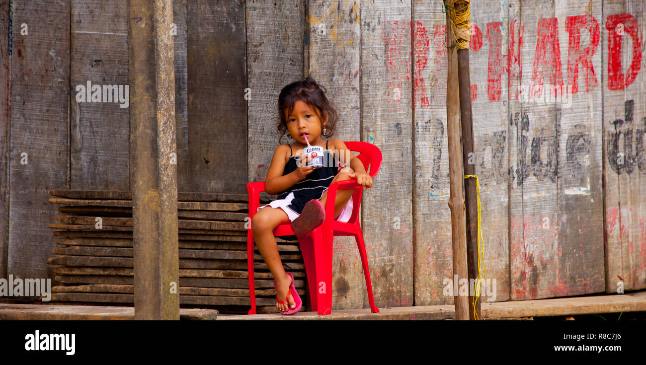 Una piccola ragazza avente un succo di frutta nella parte anteriore del legno di un piccolo negozio di Iquitos Foto Stock