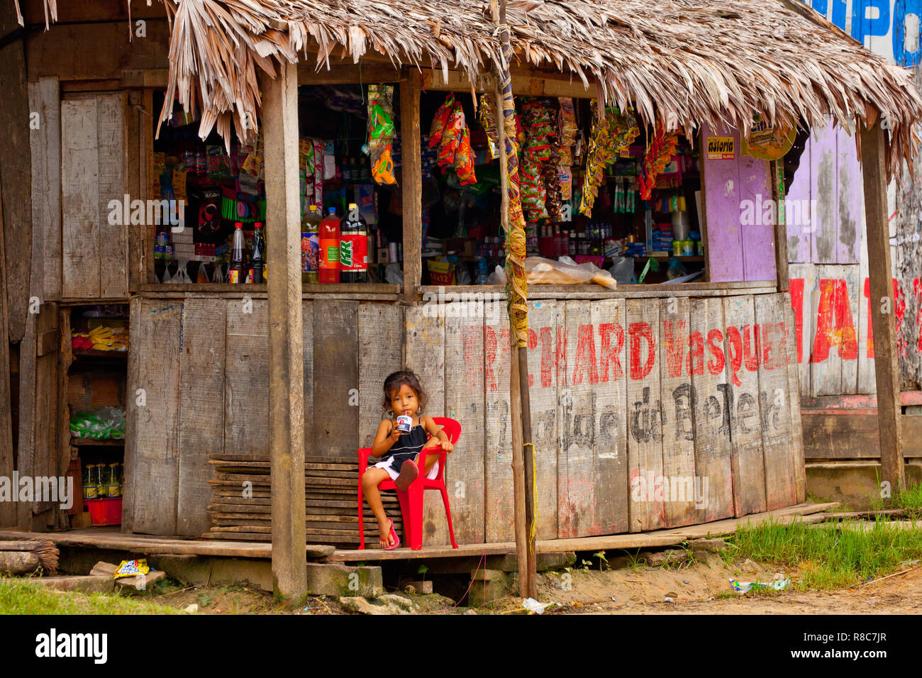 Una piccola ragazza avente un succo di frutta nella parte anteriore del legno di un piccolo negozio di Iquitos Foto Stock
