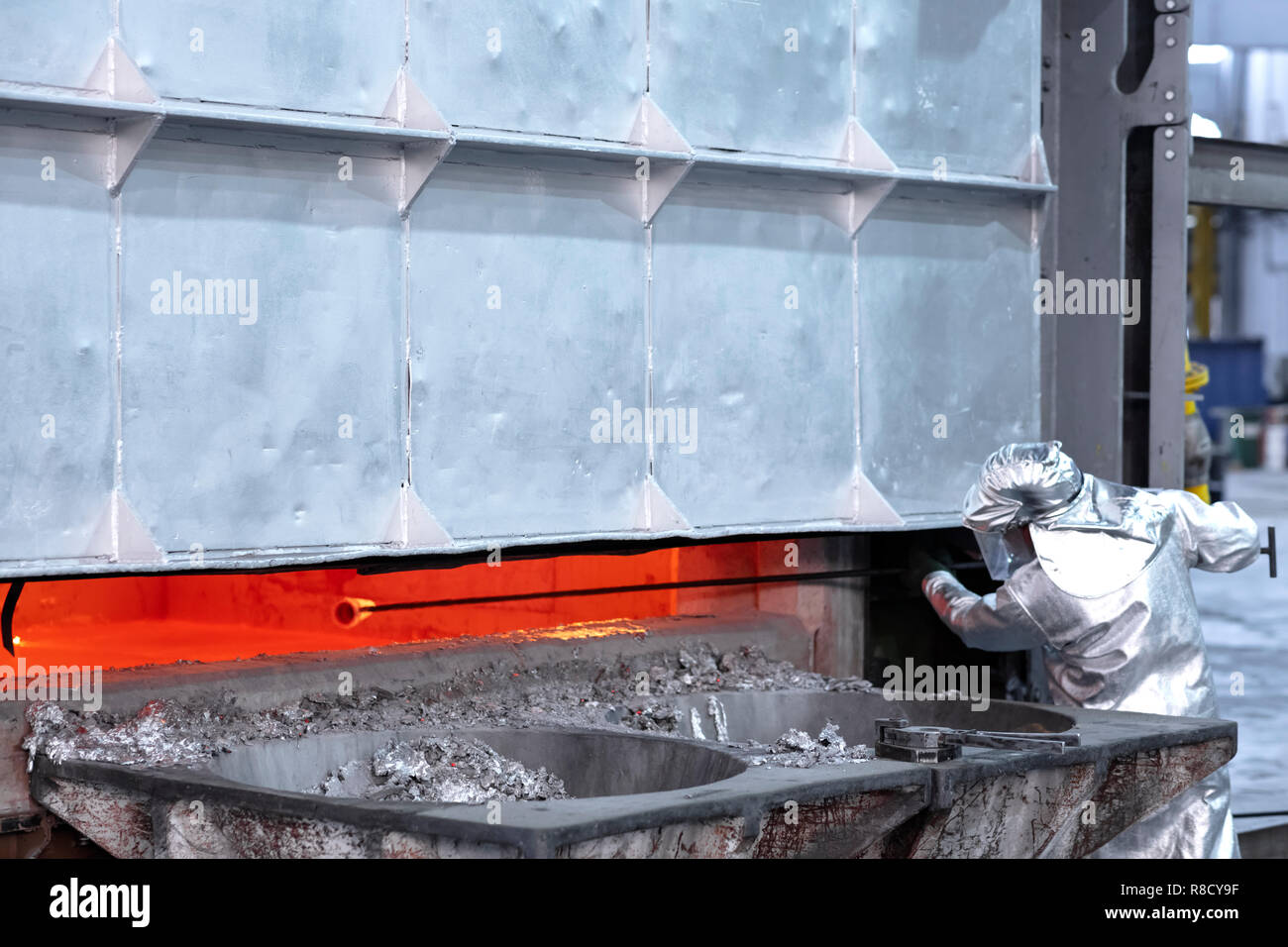 Un lavoratore il prelievo di un campione di alluminio fuso dall'interno di un forno di grande dressing il vestiario protettivo alluminò Foto Stock Un lavoratore il prelievo di un campione di alluminio fuso dall'interno di un forno di grande dressing il vestiario protettivo alluminò Foto Stock