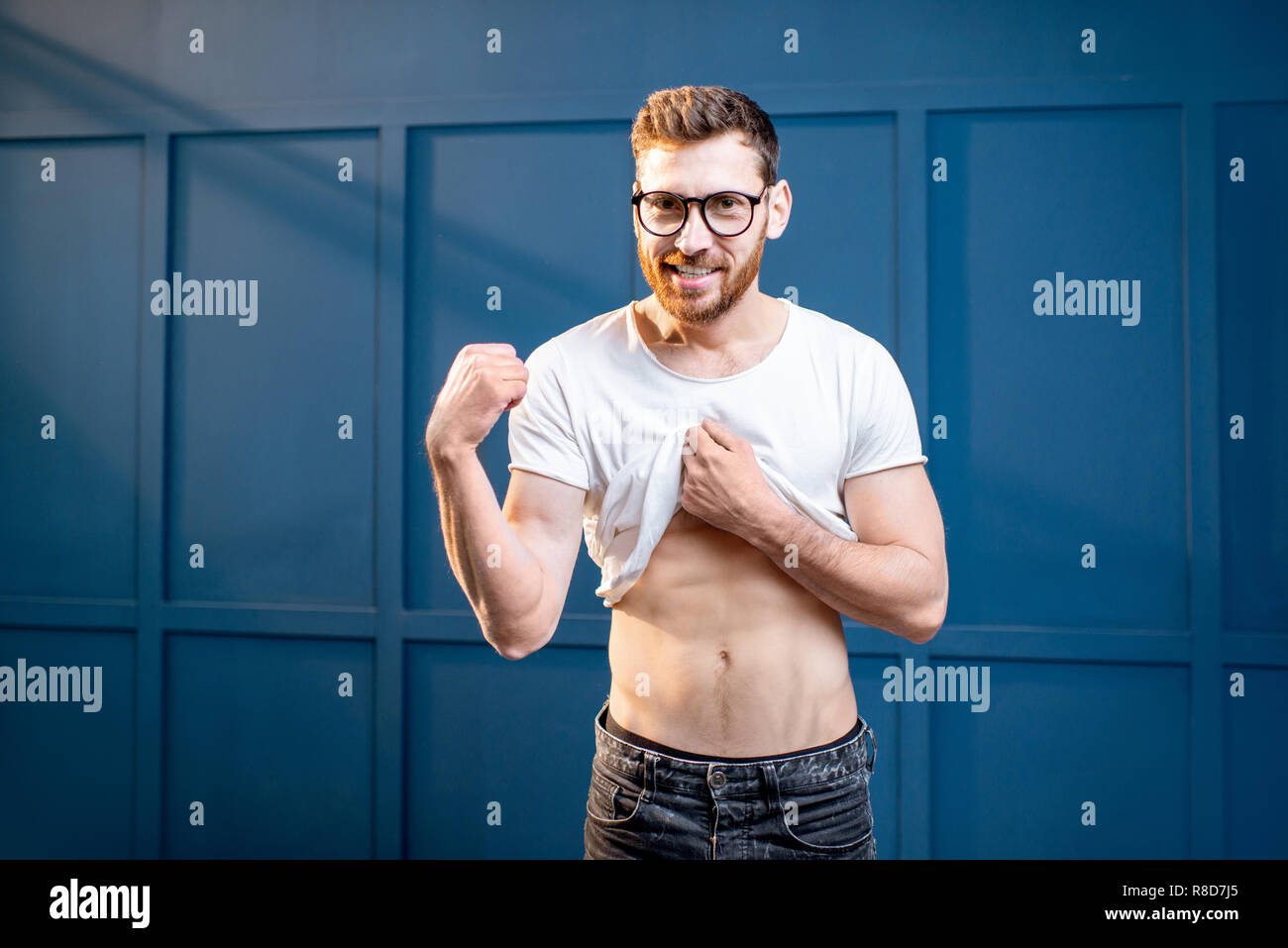 Ritratto di un bel uomo forte che mostra e bicipiti muscoli addominali sulla parete blu sullo sfondo Foto Stock