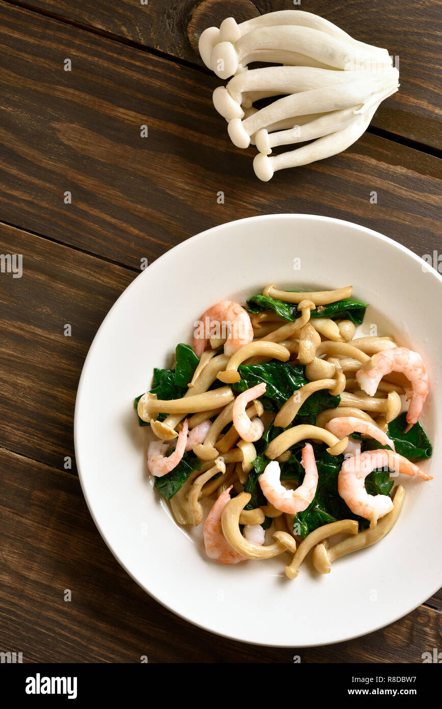 Stufati di bianco di funghi di faggio con le foglie di spinaci e gamberetti su un tavolo di legno. Vista superiore, laici piatta Foto Stock