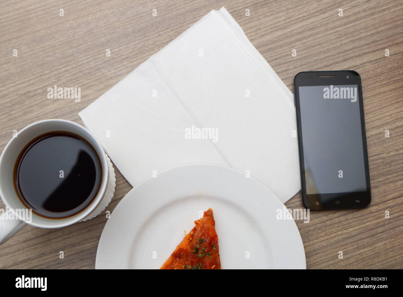 Vista superiore della scrivania, vuoto modello di carta, una tazza di caffè, la pizza e il telefono cellulare Foto Stock