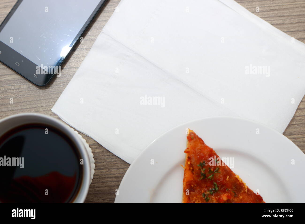 Vista superiore della scrivania, vuoto modello di carta, una tazza di caffè, la pizza e il telefono cellulare Foto Stock