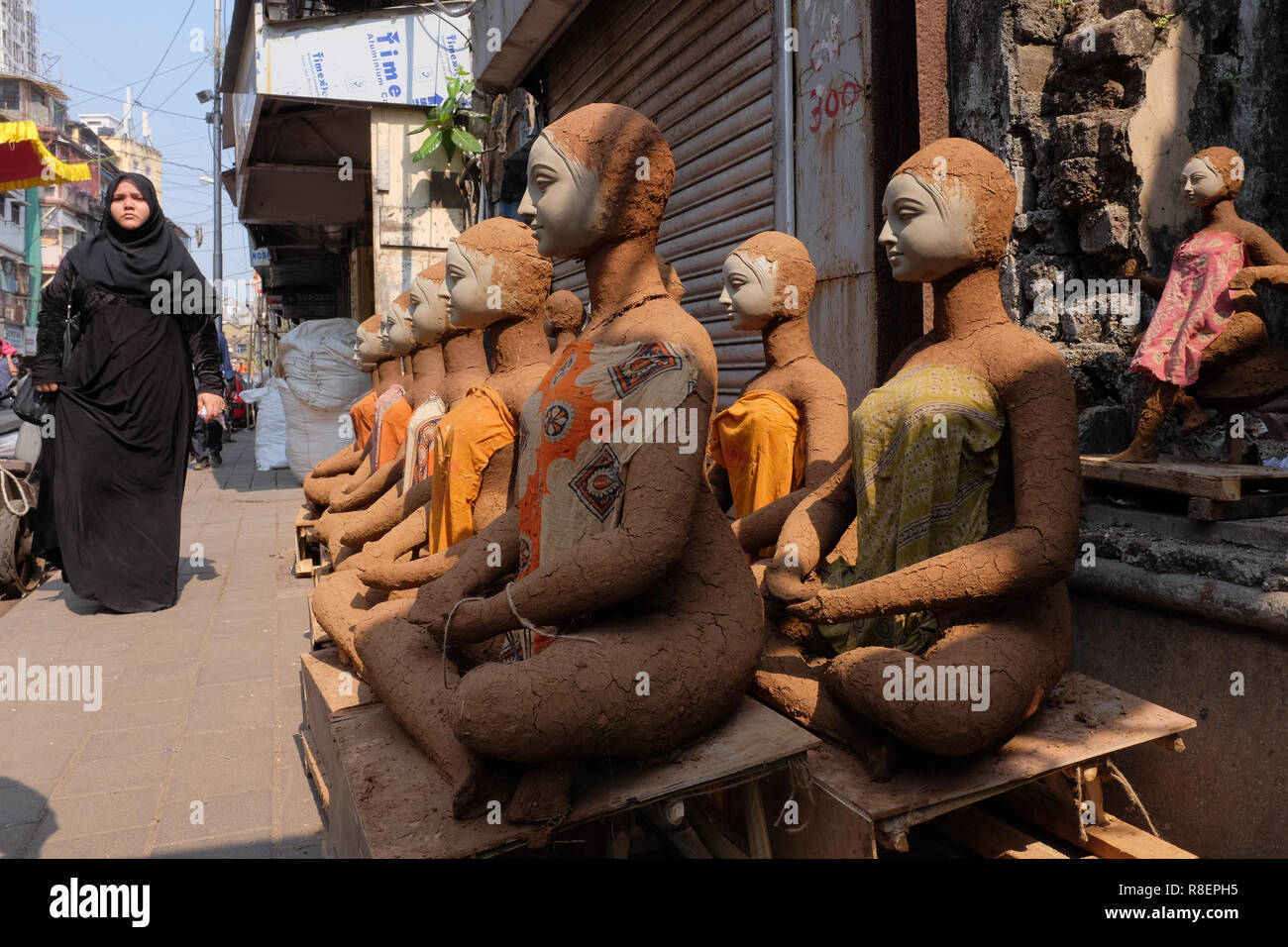 Una donna musulmana in area Gulalwadi, Mumbai, India passa appena reso creta cifre della dea Indù Durga messo fuori ad asciugare al sole Foto Stock