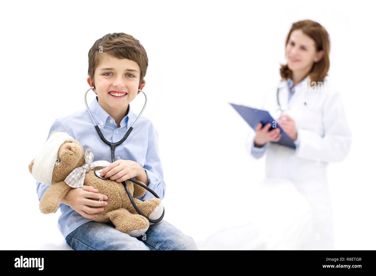 Ragazzo giochi di ruolo con Teddy bear e stetoscopio con medico in background. Foto Stock