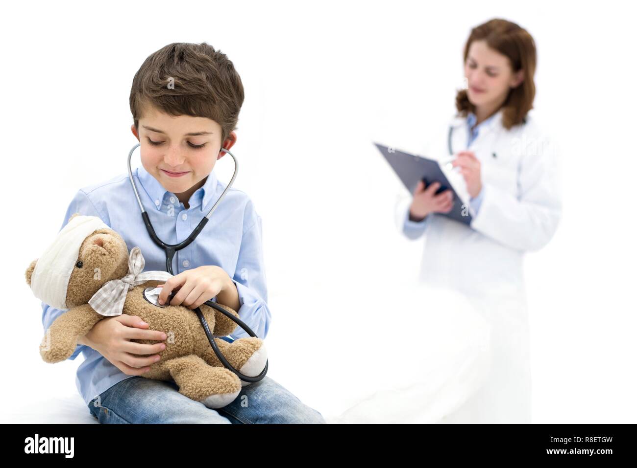 Ragazzo giochi di ruolo con Teddy bear e stetoscopio con medico in background. Foto Stock