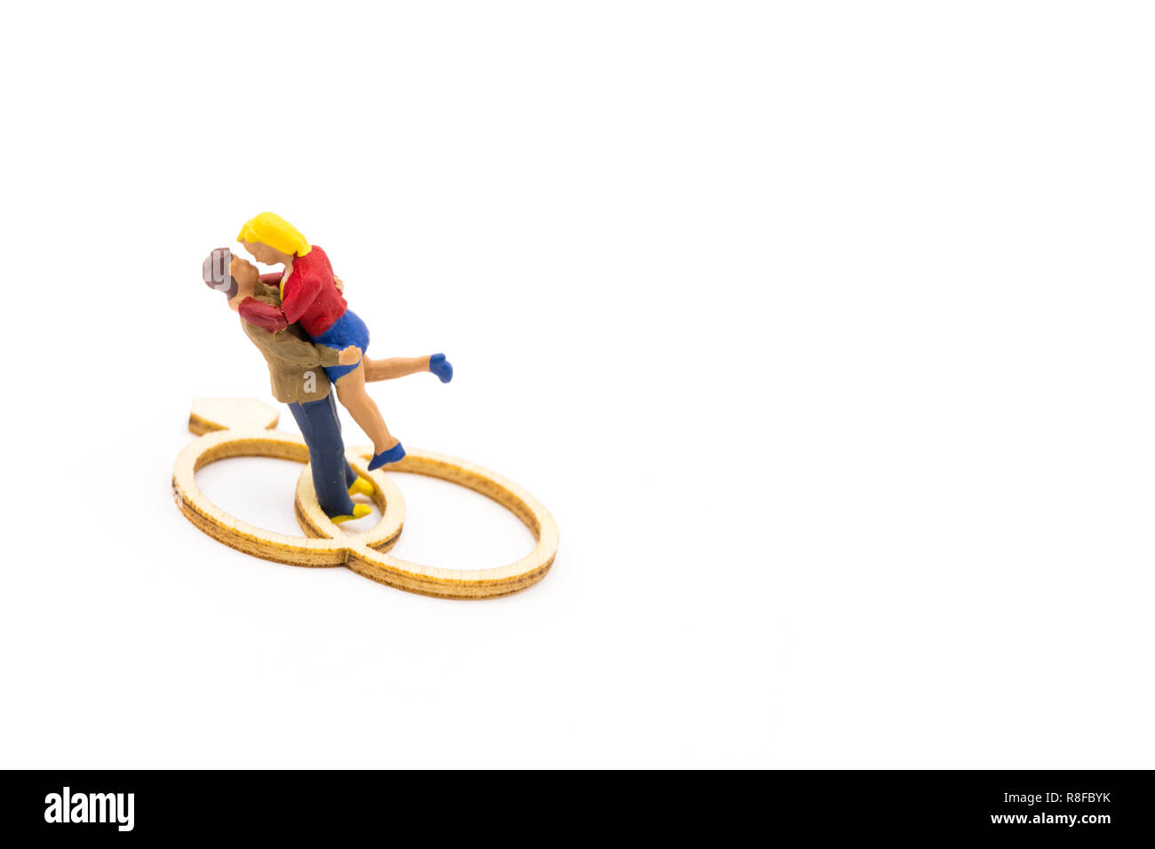 Le figure in miniatura come in amore abbracciando giovane accanto al legno anelli di nozze, isolato su sfondo bianco Foto Stock