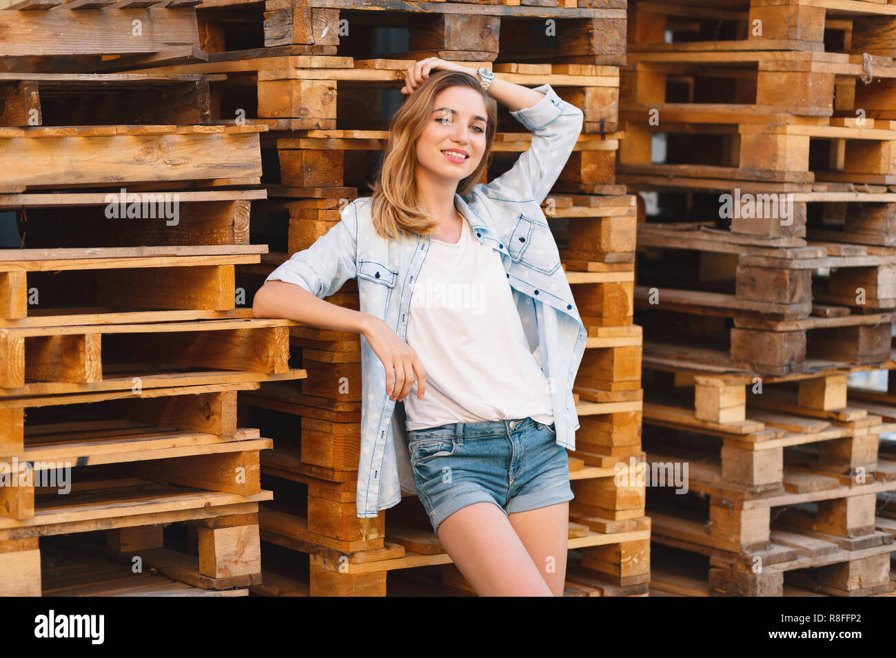 Bella ragazza sorridente, indossano jeans, pantaloncini e maglietta in posa  sul pallet legno sottofondo durante una giornata di sole Foto stock - Alamy