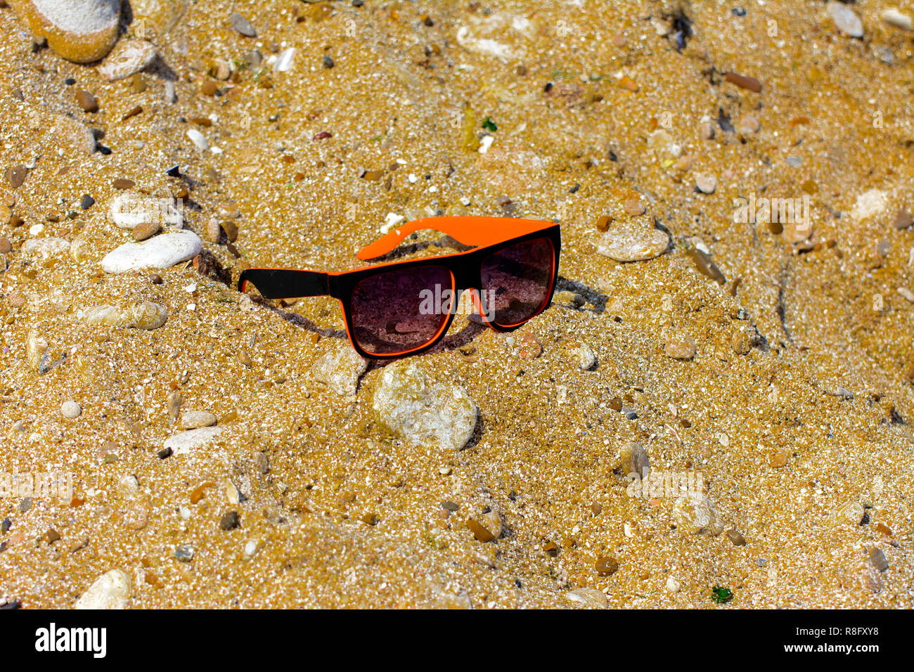 Gli occhiali da sole sono persi e giacciono sulla spiaggia in riva al mare. Nero con bordo arancione bicchieri sullo sfondo di giallo sabbia sulla riva. Gli occhiali da sole sono ri Foto Stock