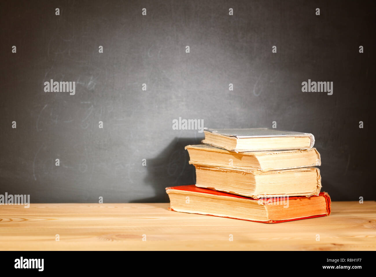 Vecchi libri scolastici giacenti su una tavola di legno a banchi di scuola di fronte a una lavagna. Il concetto di istruzione - la scrivania in auditorium Foto Stock