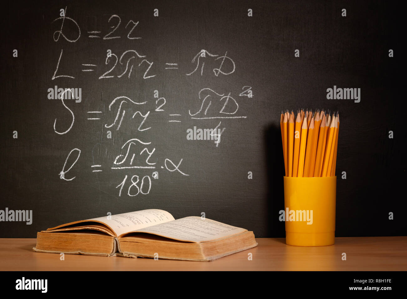 Vecchi libri scolastici e matite giacente su una tavola di legno a banchi di scuola di fronte a una lavagna nera con formule matematiche scuola. Il concetto di istruzione - il de Foto Stock