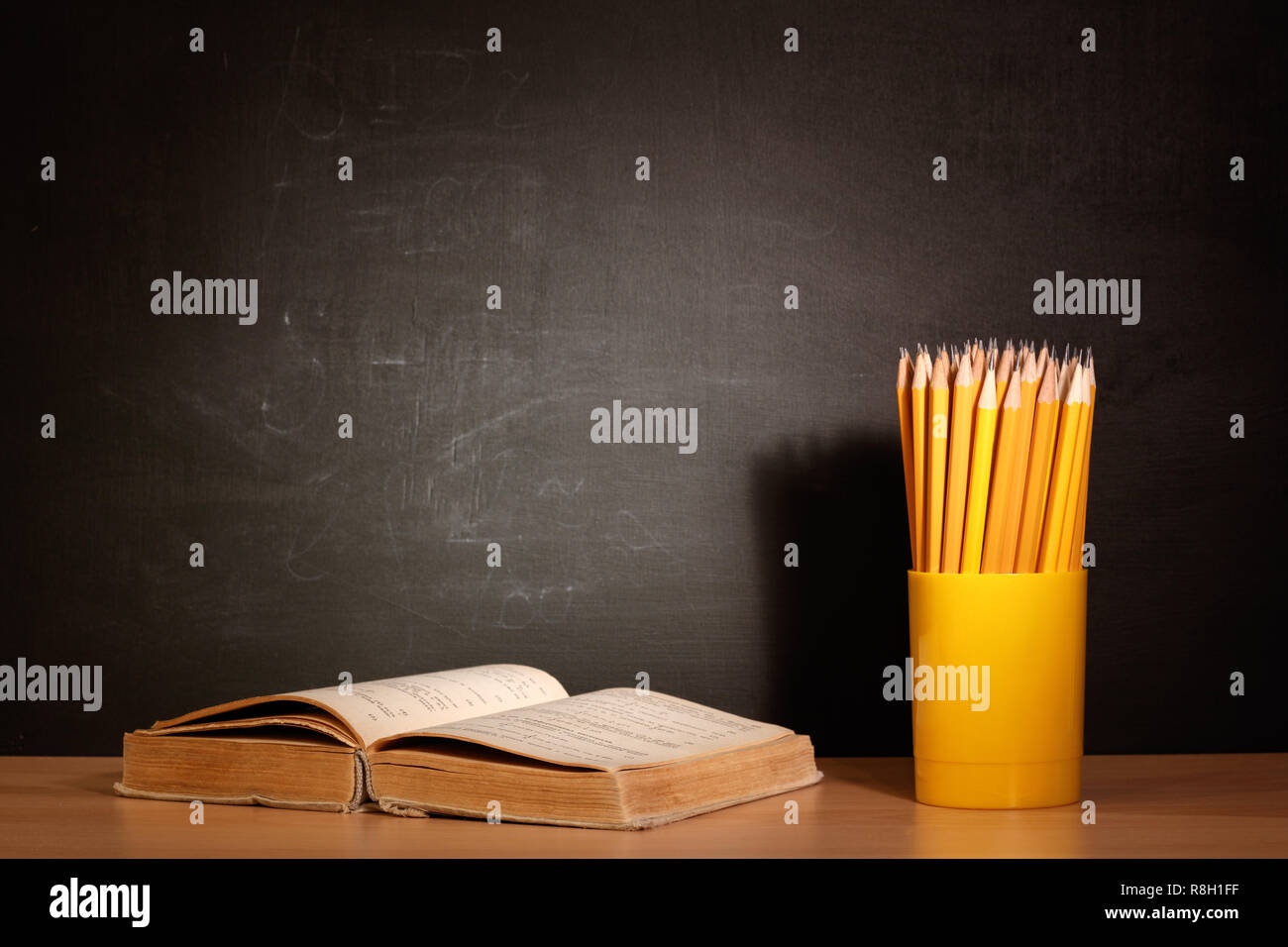 Vecchi libri scolastici e matite giacente su una tavola di legno a banchi di scuola di fronte a una lavagna scuola. Il concetto di istruzione - la scrivania in auditorium Foto Stock