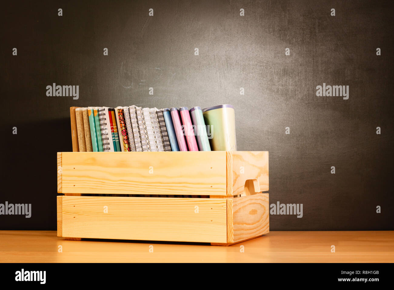 Quaderni scolastici in una fila in una scatola di legno su una tavola di legno a banchi di scuola di fronte a una lavagna. Il concetto di istruzione - la scrivania in auditorium Foto Stock