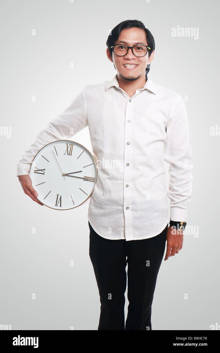 Foto immagine ritratto di un divertente giovane imprenditore asiatici sorridente in piedi e rilassarsi mentre si tiene un orologio sul suo lato, close up ritratto, il concetto di tempo Foto Stock