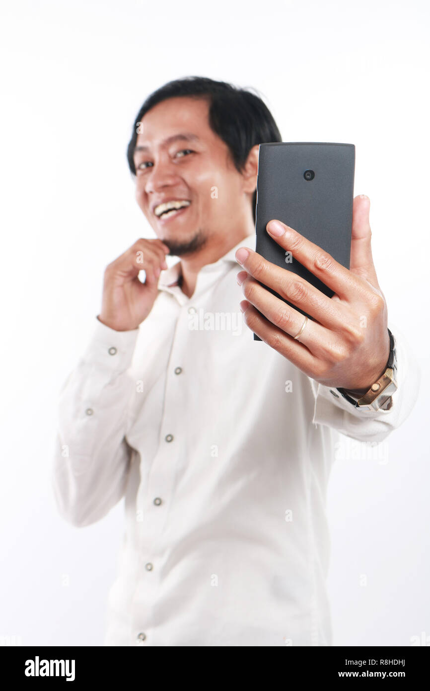 Foto immagine ritratto di un divertente giovane imprenditore asiatico sembrava felice e sorridente tenendo selfie foto di se stesso sul suo smart phone, close up por Foto Stock