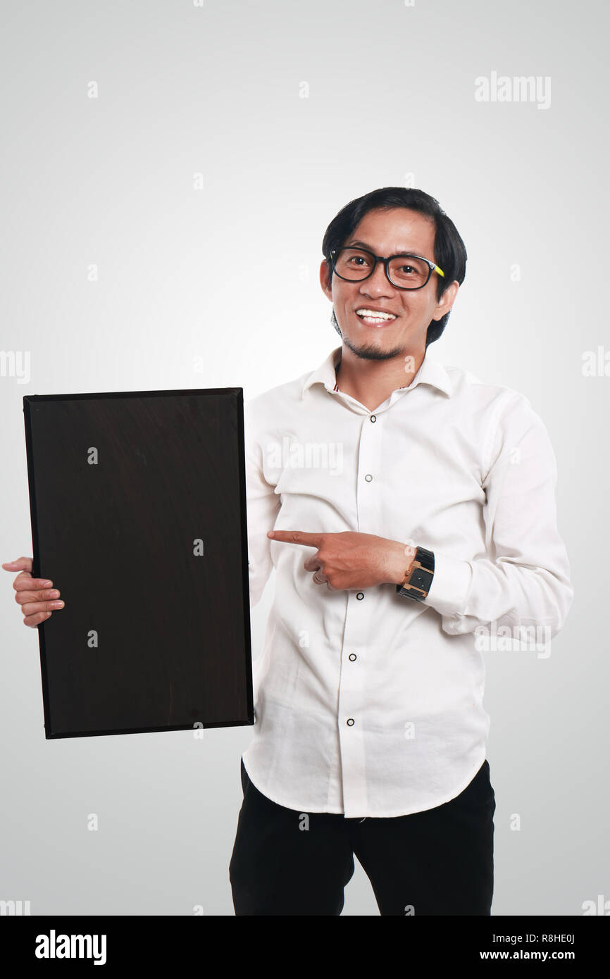 Foto immagine ritratto di funny Asian imprenditore o un insegnante o studente mostrando lavagna vuota con volto sorridente, tenendo la lavagna con una mano whi Foto Stock