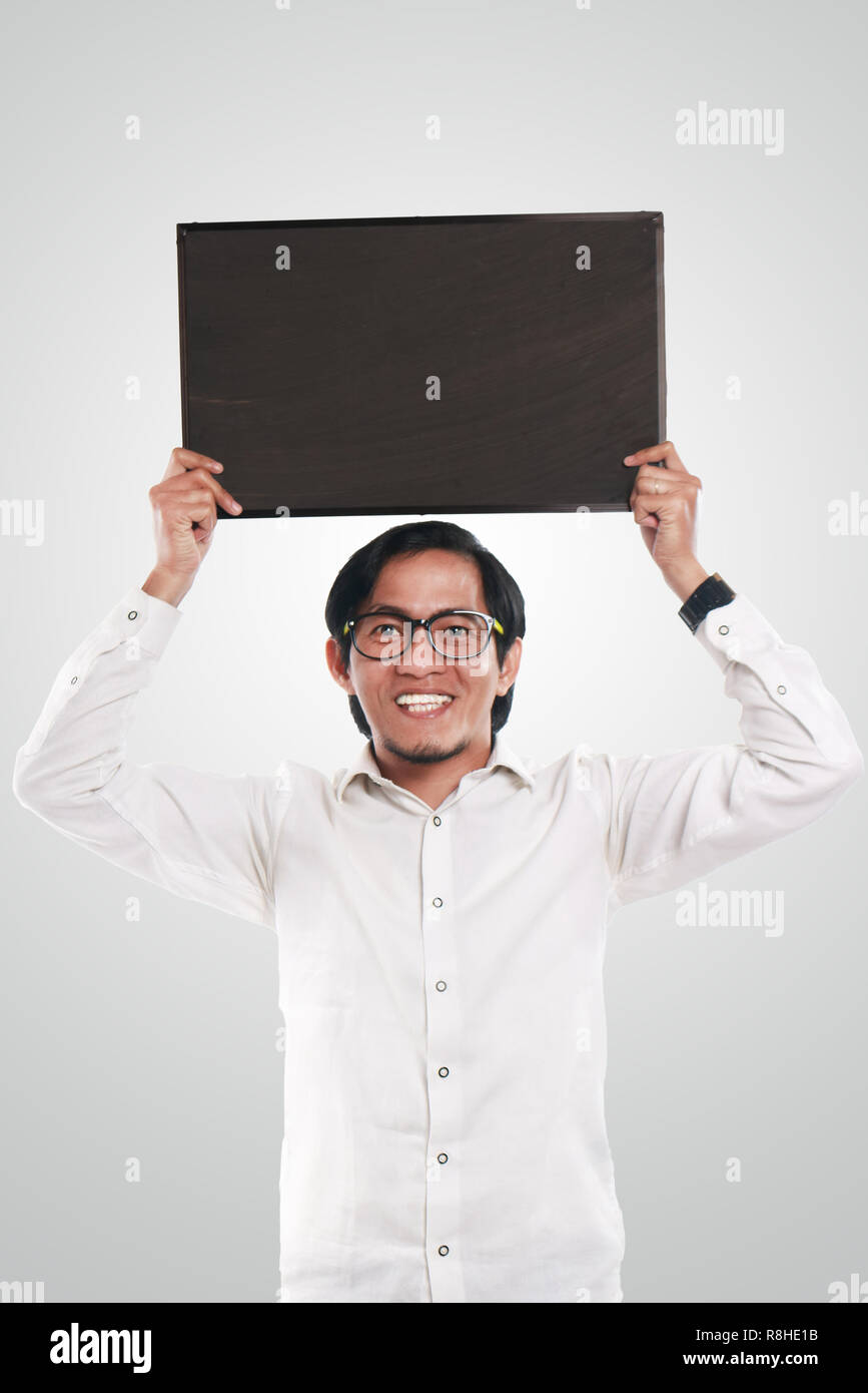 Foto immagine ritratto di funny Asian imprenditore o un insegnante o studente mostrando lavagna vuota con volto sorridente, tenendo blackboard sopra la sua testa Foto Stock