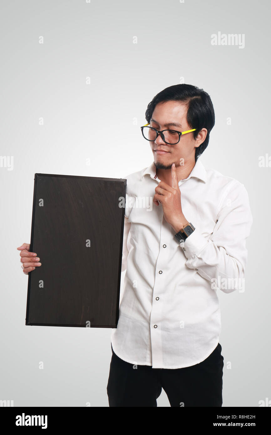 Foto immagine ritratto di funny Asian imprenditore o un insegnante o studente azienda lavagna con Viso confuso e gesto di pensiero Foto Stock