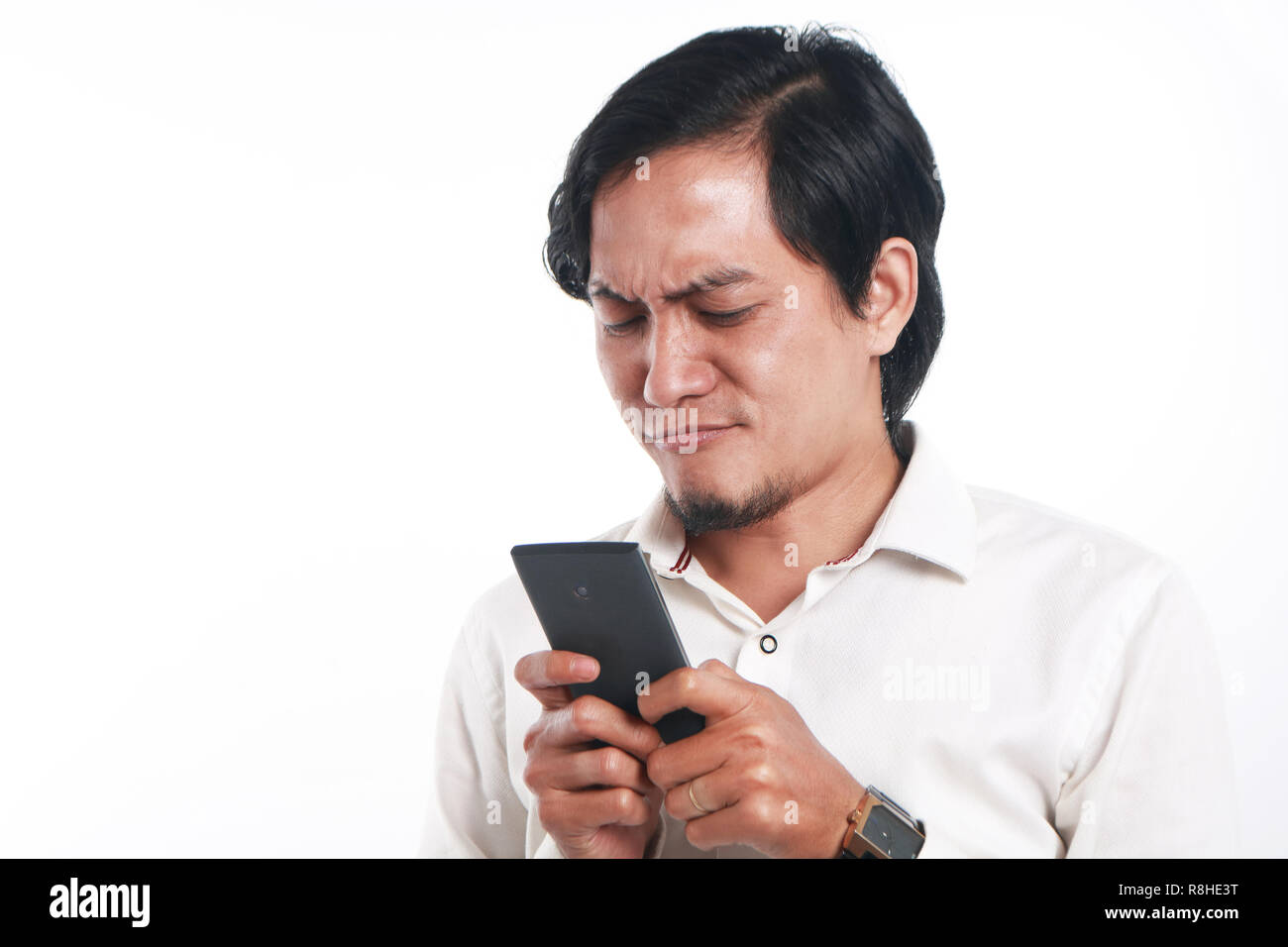 Foto immagine ritratto di un divertente giovane uomo asiatico seriamente texting sul suo smart phone. Tenendo il telefono con entrambe le mani durante la lettura del messaggio su di esso, sopra Foto Stock