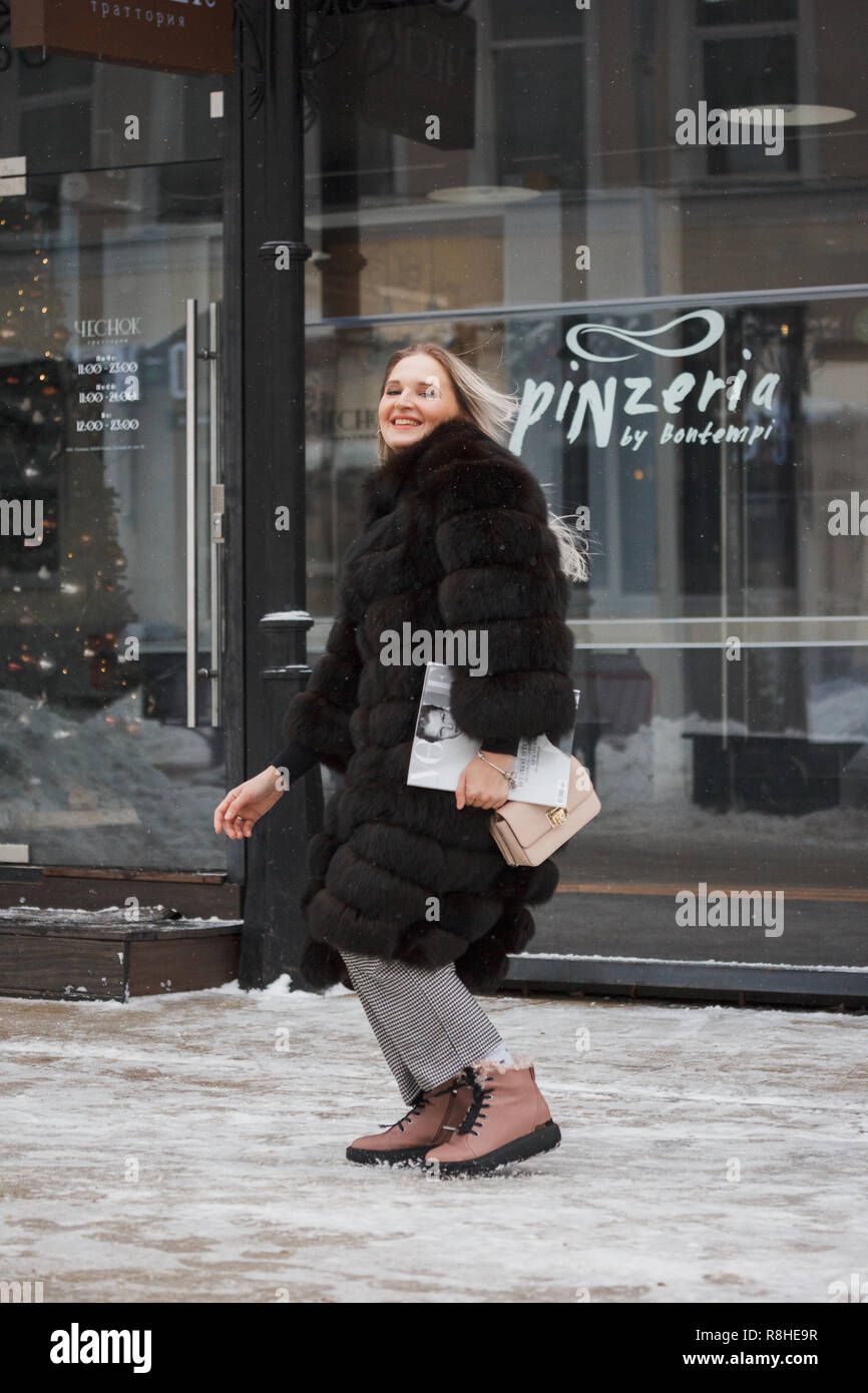 Ragazza camminare sulla neve in città strada sul marciapiede coperto di neve. Stile di vita. inverno umore, tazza di caffè, mag, Pelliccia di Visone abbigliamento. Foto Stock