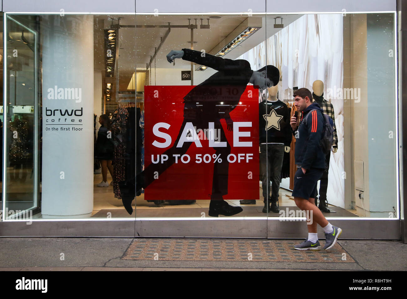 Un uomo è visto di fronte alla vetrina di un negozio visualizzando un grande 'Sale fino al 50% off' firmare su Oxford Street con 9 giorni di tempo per il giorno di Natale. I dettaglianti sono in attesa di un rush di acquirenti in piombo-fino a Natale. Foto Stock