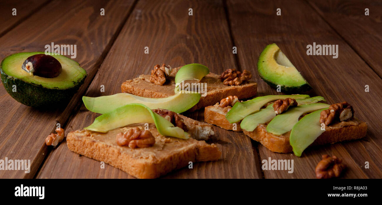 Gli avocadi e tostapane con pasta di arachidi su uno sfondo di legno. In casa la deliziosa colazione sana e toast. Foto Stock